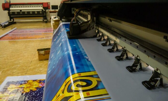 Large format printing machine in operation. Industry A wide format printer prints out a large, bright, and colorful print of a very fancy design in a clean room.
