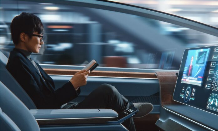 4 Ways Autonomous Cars Will Change the Industry A side view of a man in glasses and a suit sitting in the driver's seat and reading while the autonomous car drives itself.