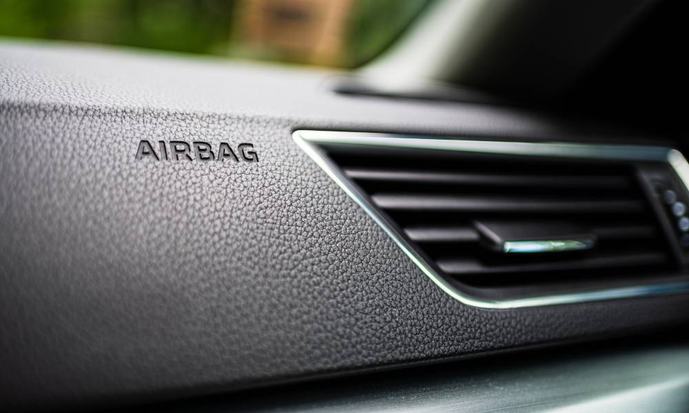 A close up of a car's dashboard and air vent with the "airbag" location engraved into the dashboard.