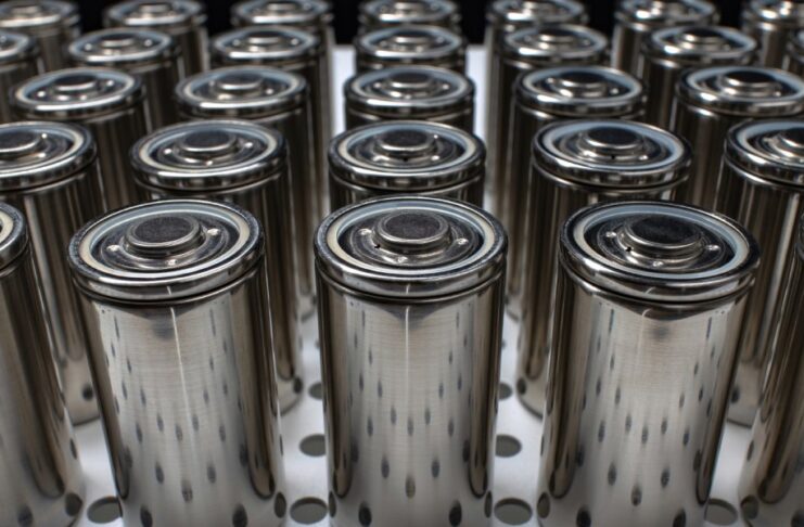 Rows of modern lithium-ion batteries with metallic casings sitting on a table with their positive sides up.