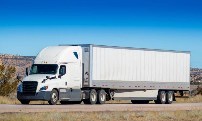 A large, industrial-grade semi-truck with a long trailer parked on the side of a remote, desert highway.