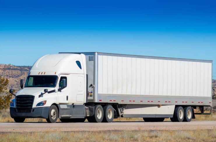 A large, industrial-grade semi-truck with a long trailer parked on the side of a remote, desert highway.