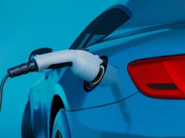 A close-up of the back of a teal electric vehicle that's charging up. The background of the image is also teal.