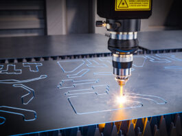 A close-up of a laser cutting torch within a CNC machine as it cuts out shapes in a piece of sheet metal.