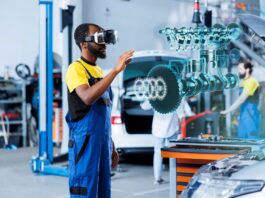 A mechanic in a repair shop uses AR to see a hologram of parts of the engine with the hood of a car up.