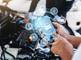 Someone is using a smartphone next to their car, which is being repaired, with technology to support the repair process.