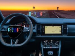 A steering wheel with a HUD is in front of a dashboard with a lit GPS. Through the windshield is a road and two signs.