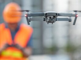 A person operating a drone with a camera attached to the equipment. They are wearing reflective construction clothes.