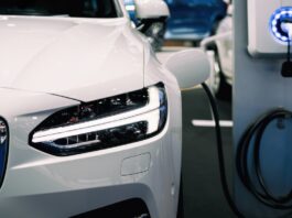 A black cable runs from a car’s driver-side fender to a charging station with glowing blue LED lights around the plug.