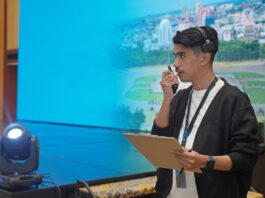 An event organizer stands by a stage set, holding a clipboard and speaking into a two-way radio to coordinate event details.