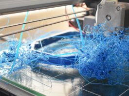 A printer bed forming the base of a failed 3D print, with the blue filament twisting into bird's nests.