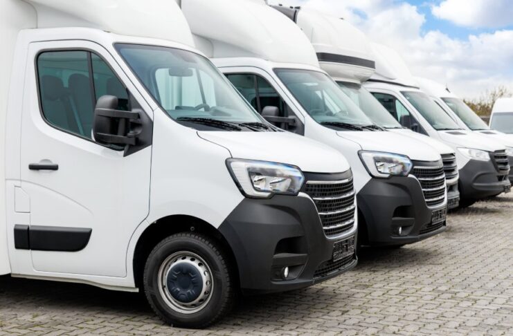 A line of white trucks parked next to each other in a business parking lot. The sky is partly cloudy behind the lot.