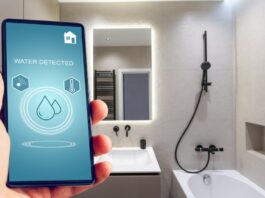 A person's hand holding a smartphone displaying the words "WATER DETECTED" in a modern bathroom with black fixtures.