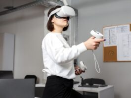 A young, creative woman engineer is testing VR glasses or goggles while standing in an empty office room.
