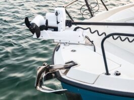A close-up of the anchor stored at the bow of a boat and the propeller system on its deck. The vessel floats in the water.