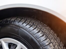 A close-up of the sun shining on a white car's tire. The tire is wet and has a fine layer of dirt on it.