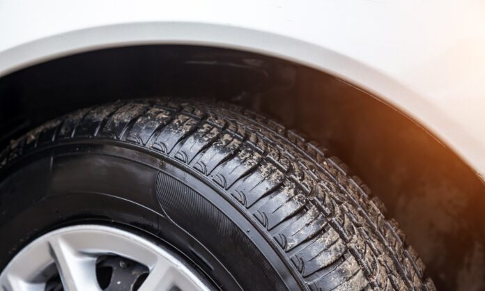 A close-up of the sun shining on a white car's tire. The tire is wet and has a fine layer of dirt on it.