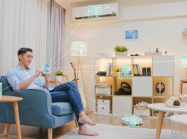 The Role of Technology in Modern Interior Design A man sits on a couch in a living room with a phone displaying graphics that connect it to different devices.