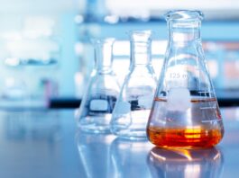 The Role of Catalysis in Sustainable Chemical Manufacturing Three glass beakers sit on a table in a laboratory. The one in front is half-filled with orange liquid.