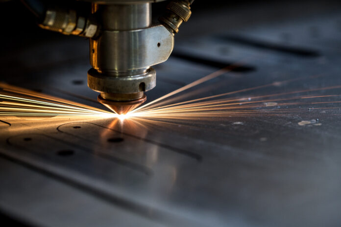 A laser precision cutting machine slices through metal, producing sparks as it forms parts for electronic components.