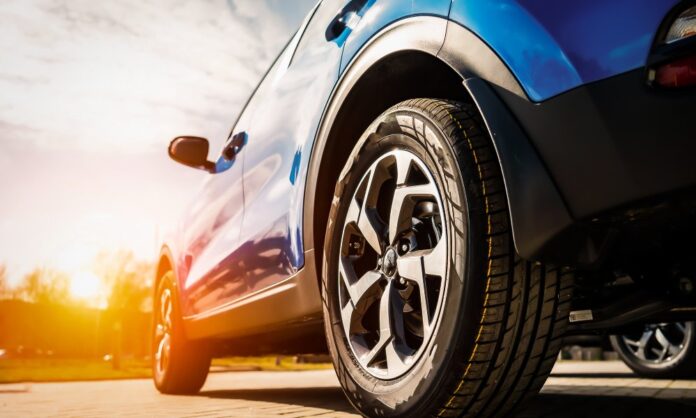 A blue car's front wheel with an alloy rim on a sunny pavement, showing modern tire and vehicle design.