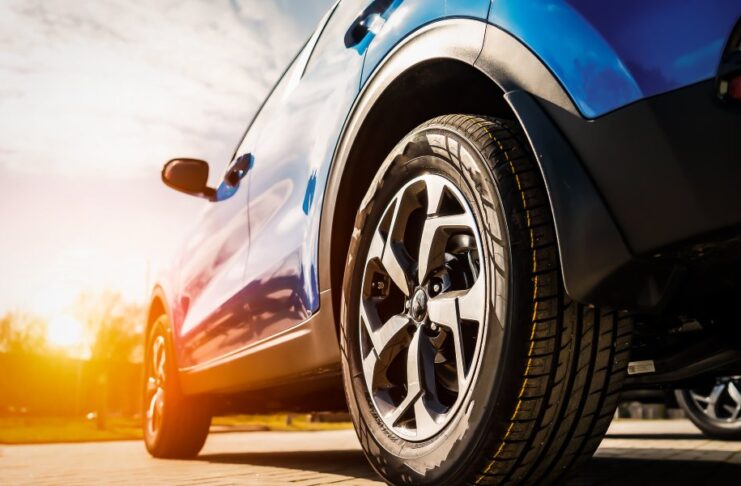 A blue car's front wheel with an alloy rim on a sunny pavement, showing modern tire and vehicle design.