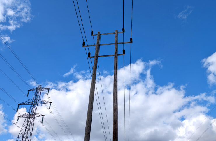 Utility poles carrying utility lines in the air. Behind a smaller wooden pole is a larger transmission system.