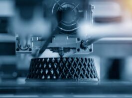 An automated 3D printing machine building a latticed structure out of black filament layer-by-layer.