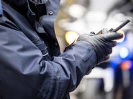 How Emergency Communication Tools Save Lives on the Road A police officer in a blue jacket and black gloves holds a two-way radio while responding at the scene of an incident.