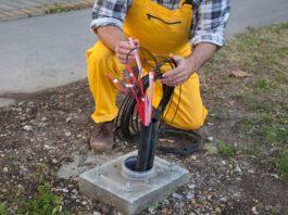 What Happens When Fiber Lines Get Damaged A fiber engineer wears a yellow overalls set as they kneel down to the fiber connection box on the ground.
