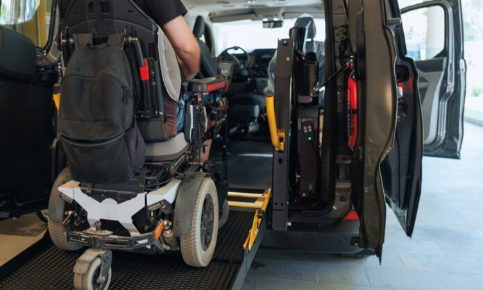 Someone in a powered wheelchair uses a rear-entry ramp to get into a vehicle. The passenger door is also open.