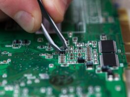 Someone using a pair of tweezers to carefully position a microchip into place on a printed circuit board.