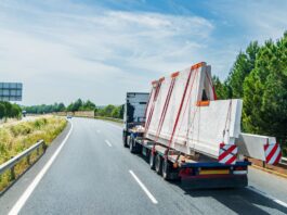 A truck with a flatbed trailer hauling an oversized load of concrete plates. The plates are strapped down to the trailer.