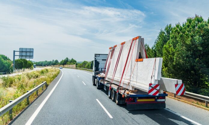 A truck with a flatbed trailer hauling an oversized load of concrete plates. The plates are strapped down to the trailer.