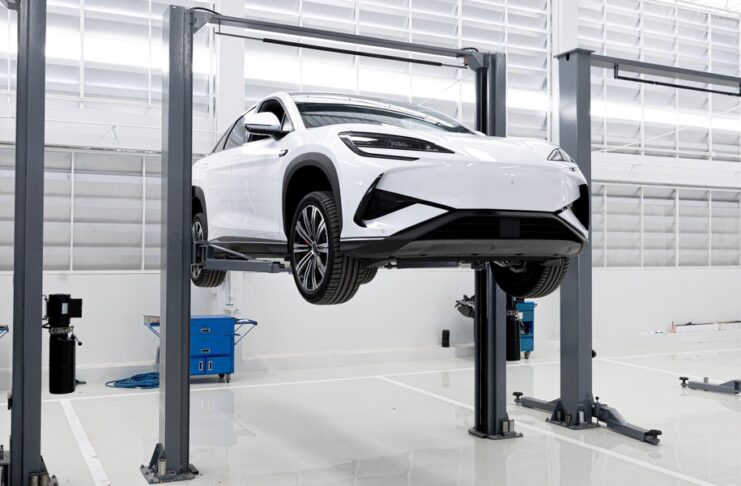 White electric SUV elevated on a hydraulic car lift inside a clean, modern automotive service garage.