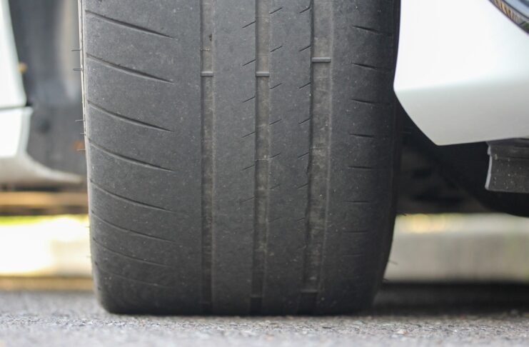 A close-up of the tire of a white car that is parked on asphalt. The tire shows uneven tread wear and faint grooves.