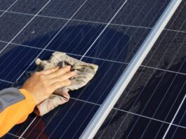 A hand wiping solar panels with a towel to clear any dust or debris. There is dust around where the rag is cleaning.