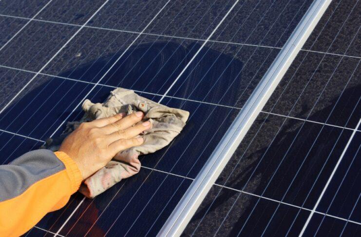 A hand wiping solar panels with a towel to clear any dust or debris. There is dust around where the rag is cleaning.