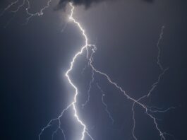 A bright lightning bolt striking through dark storm clouds in a night sky during a powerful thunderstorm.