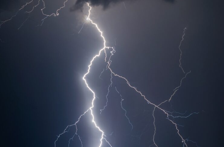A bright lightning bolt striking through dark storm clouds in a night sky during a powerful thunderstorm.