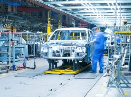The Top Trends in Automotive Manufacturing A there is ana assembly line with a partially built car. There is a man standing next to the assembly line.