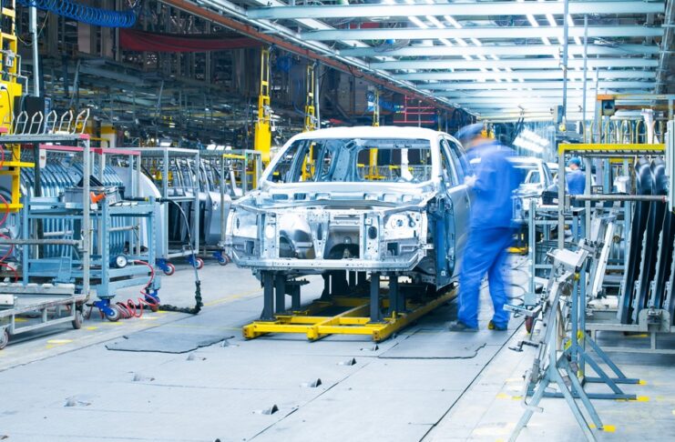 A there is ana assembly line with a partially built car. There is a man standing next to the assembly line.