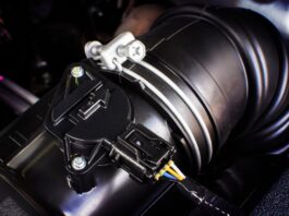 A black automotive connector with blue, yellow, and white wires attached to a black air sensor in a car.