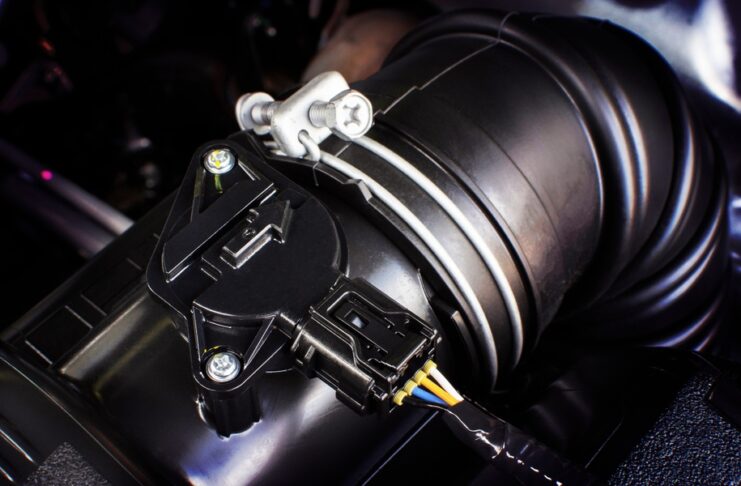 A black automotive connector with blue, yellow, and white wires attached to a black air sensor in a car.