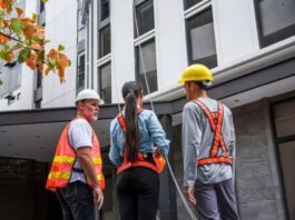 A group of engineers in safety vests and hard hats reviewing plans together at an outdoor building construction site.