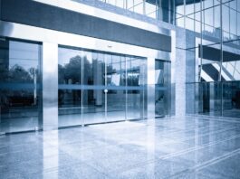 An office building entrance with automatic glass doors, metal frames, and reflective panels along the front.