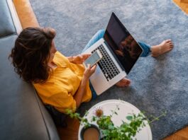 Home Internet Trends Shaping Smarter Living Spaces An aerial view of a female homeowner sitting on the floor in her living room with a laptop and her phone.