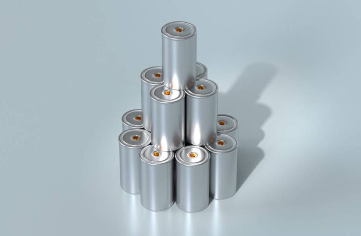 A stack of small silver lithium-ion batteries with small orange ends. The battery stack sits against a silver background.
