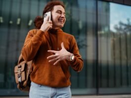 What To Check Before Backing a Gadget Startup Smiling person with a shoulder bag holds a smartphone to their ear in front of tall reflective windows.