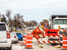 A road with heavy construction underway. Safety cones line the middle of a street with a sign saying "bump."